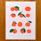 a loose grid of 12 satsumas are printed four rows of three on a white cardstock. Small simple pencil facial expressions are drawn on each, creating a range of expressions and dynamics between them. Some look away  perhaps lonely, some gazing at one another lovingly, others content and neutral. 