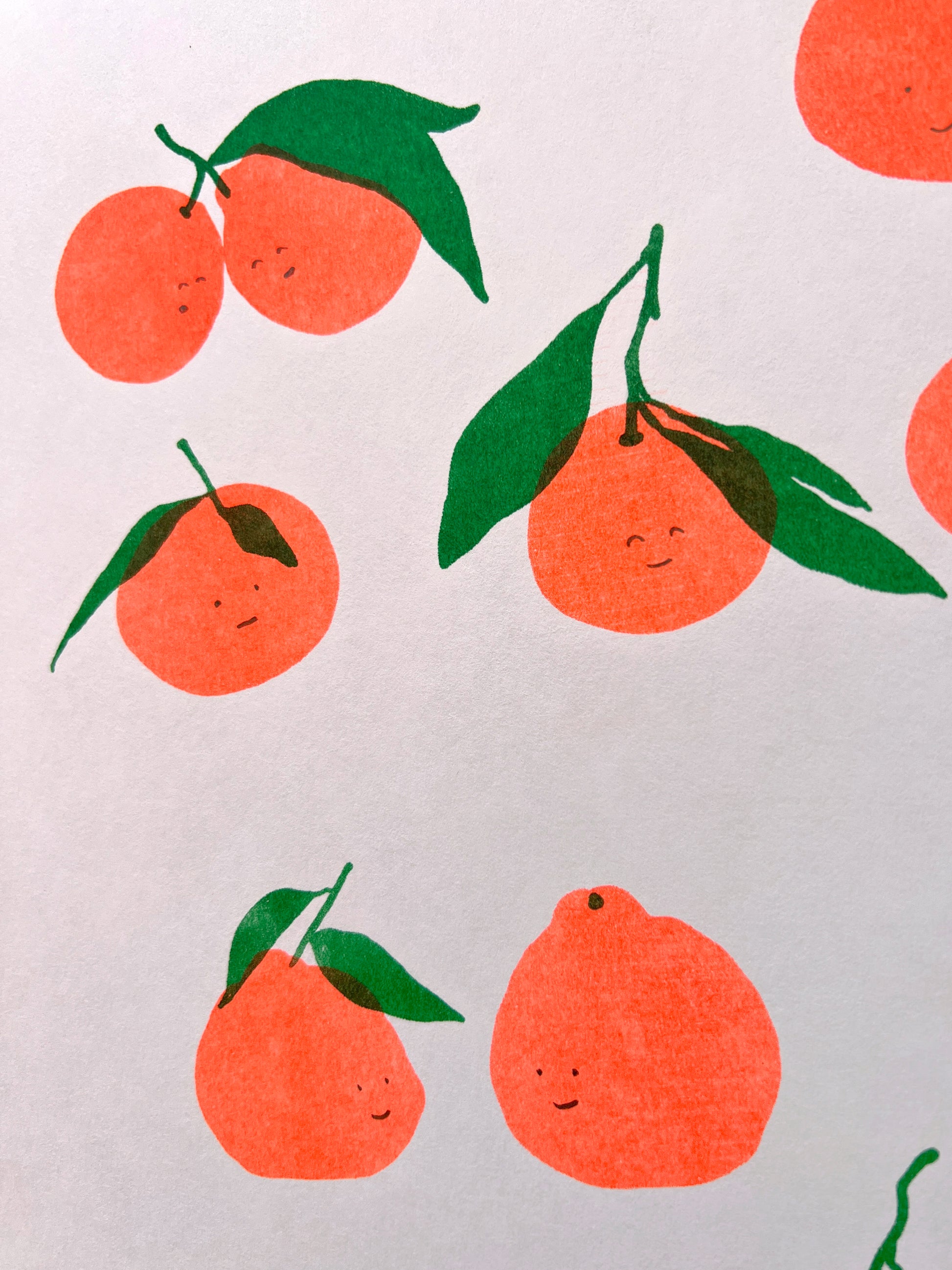 A close up of the print showing sis sets of satsumas with varying faces. In the top right corner two huddled satsumas attached by a forked stem give a closed eye smile towards one another. 