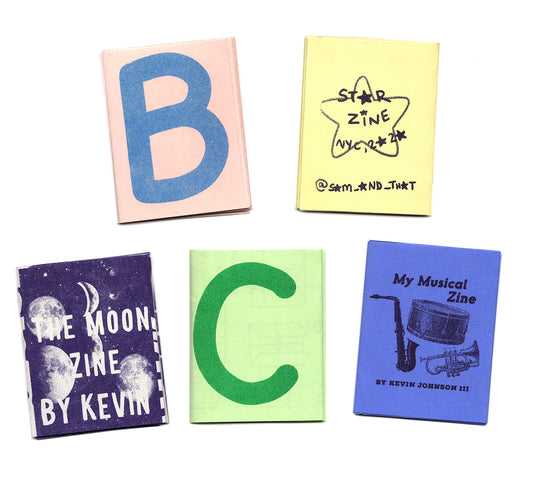 Five mini zines are laid out on a white Surface. One has a pink cover with a large blue "B", another reads "My musical Zine" with various instruments. There is a yellow "Star Zine" as well as a purple printed “Moon Zine”, and finally a simple green zine with a large "C" on the front. 
